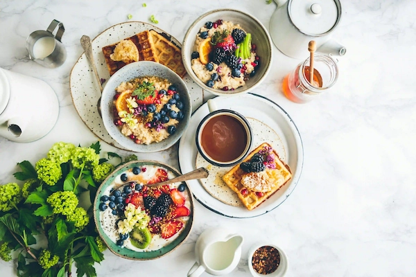 Top view of a brunch with bowls of porridge and yogurt topped with fruits and nuts