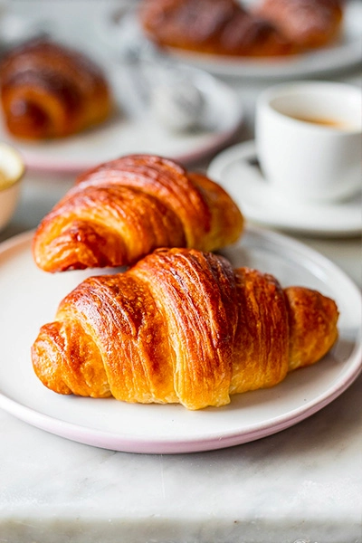 Two croissants on a plate there are 3 other croissants on a plate and a cu
