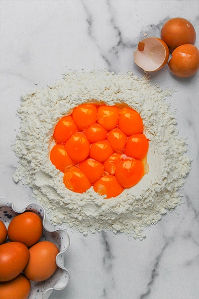 Egg yolks in the center of a mound of white flour, The scene suggests preparation for baking